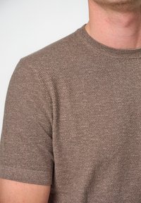 Brązowy, dziany sweter z krótkim rękawem, o fakturowanej tkaninie z prostym, okrągłym dekoltem i wykończonymi mankietami, ukazujący subtelny melanż.