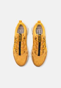 Des chaussures de sport jaunes avec une tige en mesh texturé, des lacets noirs et un onglet contrasté. Elles disposent d'une semelle blanche rembourrée pour le confort.