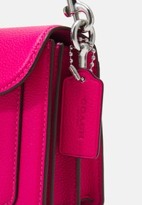 Hot pink leather handbag with a textured finish, featuring silver hardware and a branded tag attached by a ball chain.