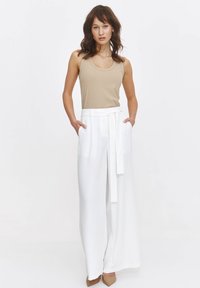 Beżowy, prążkowany top na ramiączkach połączony z białymi spodniami o szerokich nogawkach i wysokim stanem, z materiałowym paskiem i kieszeniami, o gładkiej fakturze i eleganckim fasonie.