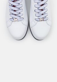 Sneaker bianche in pelle con lacci viola, con un accento in oro rosa alla base. Texture liscia e design a punta arrotondata.