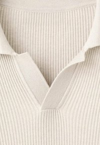 Lichtbeige geribbelde gebreide pullover met een V-hals en omgevouwen kraag. De stof is zacht met een textuur en subtiele rek.