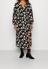 Svart och vitt djurtryck omslagsklänning med långa ärmar, en djup V-ringning, sidoslits och textilväv. Kombination med svarta ankelstövlar.