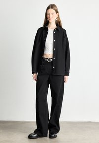 Černá denimová oversize košile se stříbrnými knoflíky, bílý krátký top, černé kalhoty s vysokým pasem a robustní černé boty, minimalistický design.