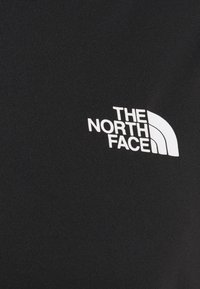 Czarna koszulka z gładkiego materiału z okrągłym dekoltem. Z przodu znajduje się białe logo "THE NORTH FACE" z zakrzywionym wzorem.