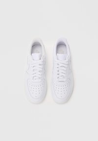 Valged spordijalatsid perforatsiooniava, ringjate paelte, pehmendatud krae ja siledast sünteetilisest materjalist. Minimalistlik disain ja logode detailid.