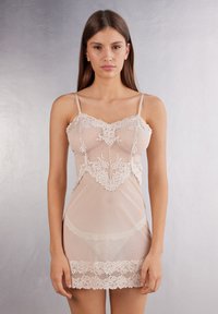 Transparante beige negligee met kantafwerking. Heeft verstelbare spaghettibandjes en een aansluitend lijfje met een bloemenkantpatroon aan de zoom.