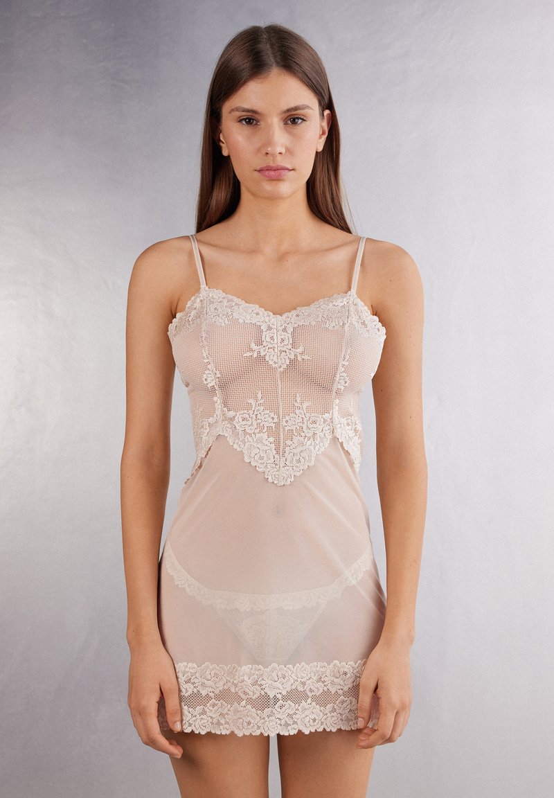 Transparante beige negligee met kantafwerking. Heeft verstelbare spaghettibandjes en een aansluitend lijfje met een bloemenkantpatroon aan de zoom.