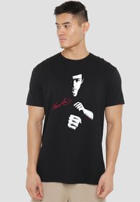Black cotton t-shirt featuring a graphic of Bruce Lee's face and fists in white, with "Bruce Lee" text in red underneath the image.