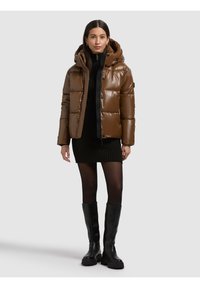 Giubbotto imbottito marrone con finitura lucida, cappuccio e dettagli neri. Indossato sopra un vestito nero testurizzato e abbinato a stivali neri al ginocchio.