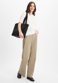 Witte gebreide trui met textuur, beige wijde broek, zwarte tote bag met stoffen oppervlak en zwarte loafers met gouden hardware accenten.