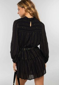 Vestido negro con rayas doradas, mangas largas y falda con volantes. Presenta una espalda con apertura en forma de ojal, cuerpo fruncido y un cinturón negro con detalles dorados.