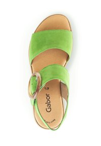Sandalo verde in suede con due ampie cinghie e un accento circolare in legno sulla caviglia. Presenta una suola imbottita color marrone chiaro.