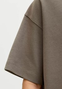 Siva bombažna majica z ohlapnim krojem, okroglim izrezom in kratkimi rokavi. Ima gladko teksturo in dvojno šivano spodnjo obrobo.