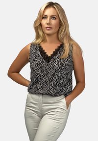Czarny i biały wzorzysty top bez rękawów z dekoltem w serek i koronkowym wykończeniem, zestawiony z jasnobeżowymi, dopasowanymi spodniami. Gładki materiał i luźny krój.