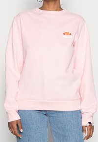 Felpa rosa con maniche lunghe, polsini e orlo a coste, con un piccolo logo arancione e bianco sul petto. Materiale morbido in misto cotone.