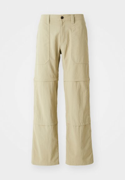Pantalons cargo beiges avec une conception à jambe droite, deux poches avant et un ourlet zippé pour une longueur ajustable. Fabriqués en tissu léger.