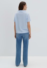 Hellblaues Kurzarmshirt mit texturiertem Muster, kombiniert mit weit geschnittenen blauen Jeans. Das Outfit hat einen schlichten Kragen und eine lockere Passform.