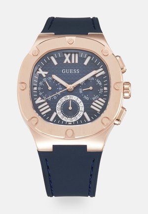 Montre chronographe en ton or rose avec un cadran texturé bleu marine, de grands numéros romains et un bracelet en silicone bleu marine durable. Plusieurs sous-cadrans inclus.