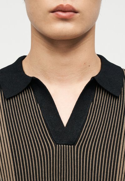 Gros plan sur le cou et les lèvres d'une personne portant une chemise noire à col avec de fines rayures verticales beige.