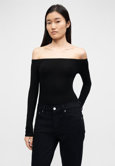 Black off-the-shoulder long-sleeve bodysuit made of smooth fabric, paired with high-waisted dark jeans featuring silver hardware details.