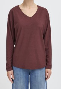 Weinrote Langarm-V-Ausschnitt-Bluse aus weichem Stoff, mit lockerer Passform und Raglanärmeln, kombiniert mit hellblauen weiten Jeans.