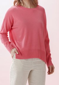 Rosa Pullover mit Rundhalsausschnitt, gerippten Bündchen und Saum; weiche Textur mit lockerem Sitz, ergänzt durch hellbeige Leinenhosen.