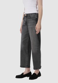 Czarne dżinsy o szerokich nogawkach z wyblakłą strukturą, pięcioma kieszeniami i zapięciem na guzik, stylizowane z bezrękawnym białym topem i czarnymi mokasynami.