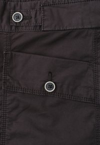 Gros plan d'une poche en tissu foncé avec deux boutons ronds noirs et des détails de couture visibles sur un vêtement.