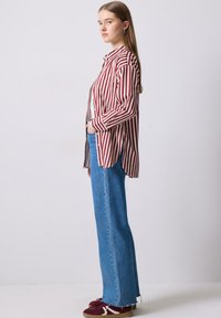 Camicia a righe rosse e bianche con maniche lunghe, abbinata a jeans a gamba dritta chiari a vita alta e scarpe da ginnastica bordeaux.