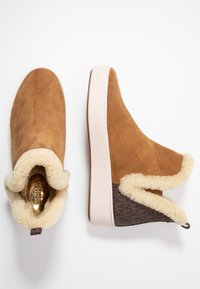 Bottines en daim marron avec un col en fausse fourrure crème, une semelle blanche lisse et un panneau texturé marron à l'arrière.