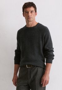 Dunkelgrauer gestrickter Pullover mit Rundhalsausschnitt, gerippten Bündchen und entspannter Passform, kombiniert mit Nadelstreifenhose.