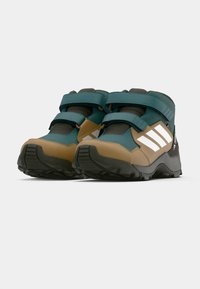 Mid-cut hiking shoes featuring a teal, grey, and tan color scheme, with Velcro straps, textured upper, and rugged outsole for traction.