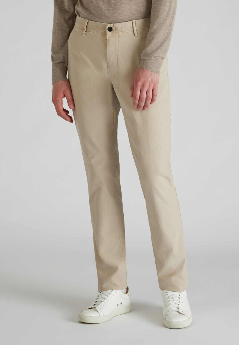 Chino in cotone beige con vestibilità dritta, dotati di chiusura con bottone frontale e tasche laterali, abbinati a sneaker bianche.