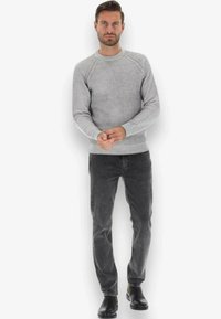Maglione grigio a coste con colletto rotondo e maniche raglan, abbinato a jeans grigio scuro e stivali neri alla caviglia.