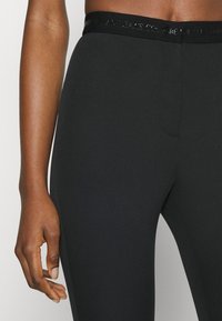 Zwarte leggings met een gladde textuur, voorzien van een brede tailleband met verhoogde branding. Het ontwerp bevat een voorste naaddetail.