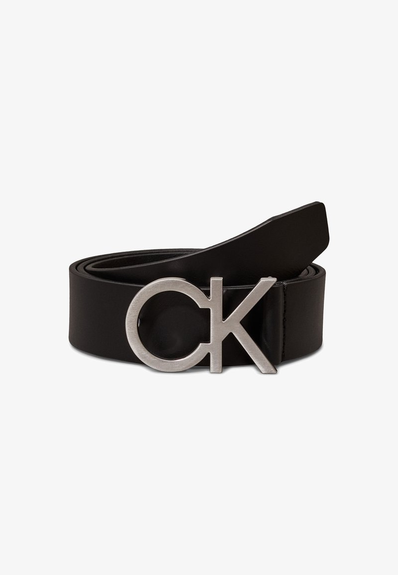 Svart skinnbelte med bred reim og en rund sølvfarget metallspenne med initialene "CK." Glatt tekstur med et moderne design.
