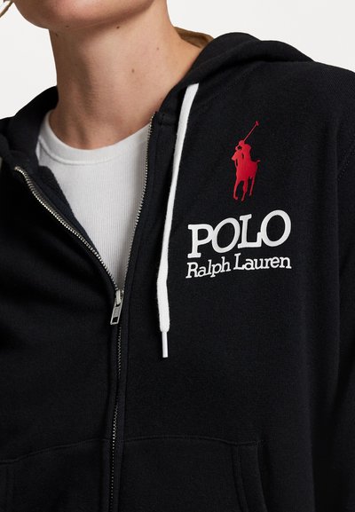 Čierna mikina na zips s bielymi šnúrkami. Obsahuje veľké biele logo "POLO" a vyšitú siluetu jazdca v červenej farbe na hrudi.