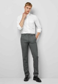 Weißes Hemd mit Knöpfen und graue Hose, taillierte Passform. Glatte Stoffqualität, minimale Muster. Schwarze Schuhe runden das Outfit ab.