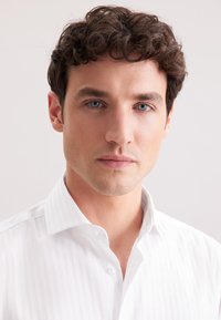 Camicia a righe bianche con colletto button-down, caratterizzata da una texture liscia. La camicia è indossata da un modello con capelli corti e ricci.