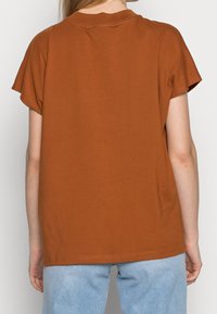 Maglietta a maniche corte marrone con scollo rotondo e vestibilità rilassata, abbinata a jeans in denim azzurro chiaro. Tessuto morbido e design casual.