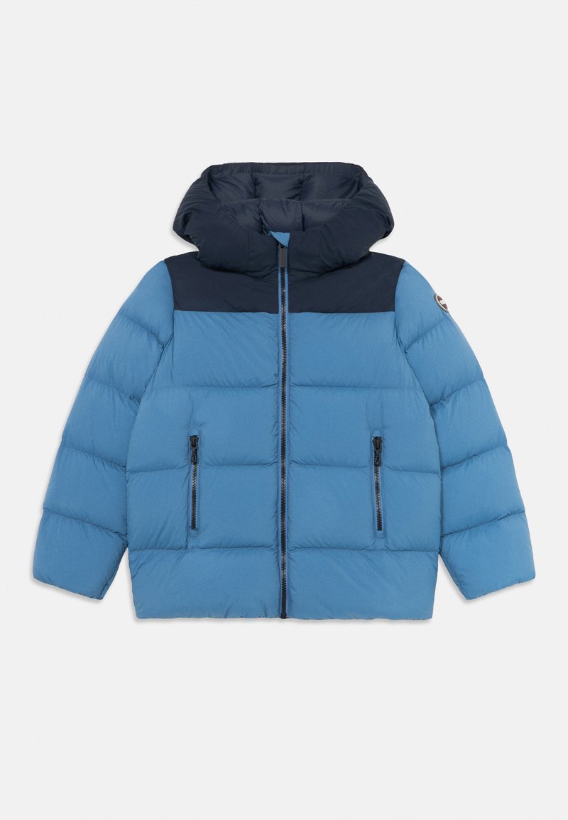 Casaco puffer azul com yoke e capuz em azul-marinho, fecho frontal, dois bolsos com zíper e patch do logótipo na manga, disposto em plano sobre fundo branco.