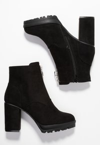 Botines de ante negros con puntera redonda, parte superior texturizada, cremallera lateral y un tacón grueso y estriado para mayor tracción.