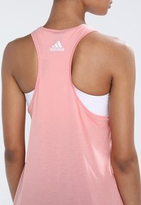 Canotta sportiva rosa con design a schiena scoperta, texture morbida e logo Adidas ricamato di colore bianco sulla parte alta della schiena.