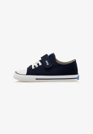Zapatilla de lona navy con puntera y suela de goma blanca. Presenta un diseño de cordones, una correa de Velcro y detalles azules en la lengua y el talón.
