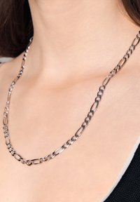 Srebrny metalowy naszyjnik z wydłużonymi ogniwami o przemiennych kształtach, gładkiej fakturze i minimalistycznym wzornictwie.
