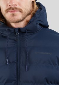 Marineblaue Daunenjacke mit Reißverschluss, verstellbarer Kapuze und Zugkordeln. Hergestellt aus glänzendem, gestepptem Material. Mit Logo auf der Brust.
