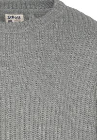 Szary sweter z okrągłym dekoltem. Teksturowana tkanina zdobiona jest prążkowaniem oraz metką z informacjami o marce.