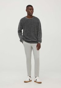 Maglione a righe bianco e nero con scollo rotondo, abbinato a pantaloni slim-fit grigio chiaro e sneakers bianche con suola marrone.