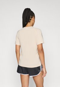 Lichtbeige sportshirt met korte mouwen, ronde hals en een gladde textuur, gecombineerd met zwarte shorts met witte accenten.